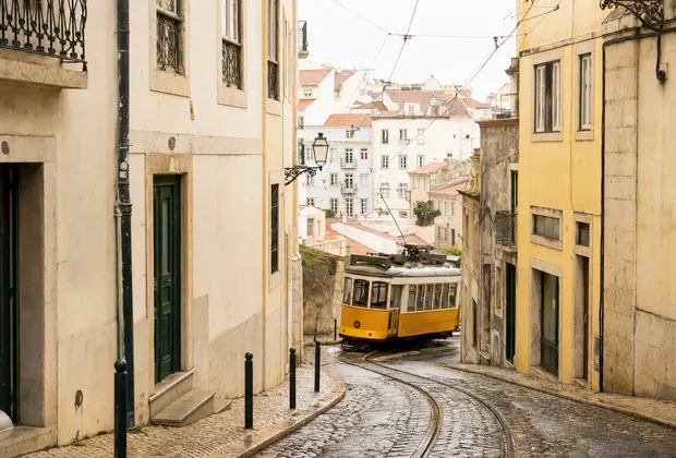 A yellow tram turning through a quiet Lisbon street after rain